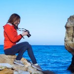 Mujer joven con cámara de fotos dslr, mar de verano y blus cielo fondo