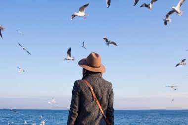 Şapkalı genç kadın stand sonbahar plaj n güneşli gün ve martılar izlerken