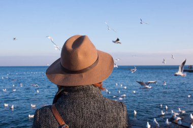 Şapkalı genç kadın stand sonbahar plaj n güneşli gün ve martılar izlerken