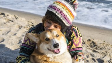 Genç ve mutlu bir kadın, sonbahar güneşli sahilde şirin bir Corgi sosisliyle yürüyor.