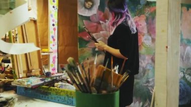 Büyük resim atölyesinde çalışan sanatçı, renkli saçlı hippi kadın ressam.