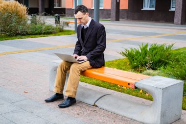 İş adamı dışarıda bilgisayar ve cep telefonuyla çalışıyor.