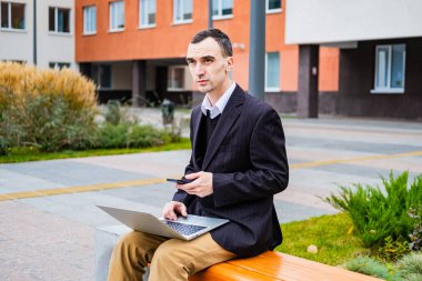 İş adamı dışarıda bilgisayar ve cep telefonuyla çalışıyor.