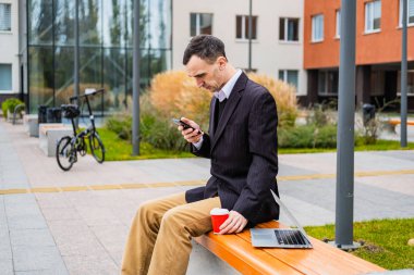 İş adamı dışarıda bilgisayar ve cep telefonuyla çalışıyor.