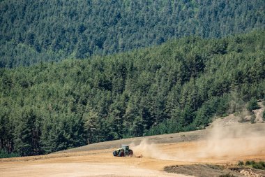 Traktör ormanın yakınındaki tarlayı sürüyor.