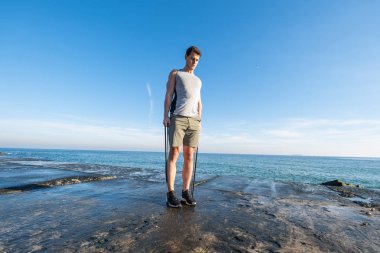 Young fit male training with  athletic rubber on the beach in summer day