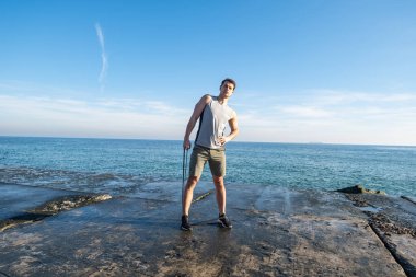 Young fit male training with  athletic rubber on the beach in summer day