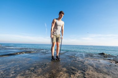 Young fit male training with  athletic rubber on the beach in summer day