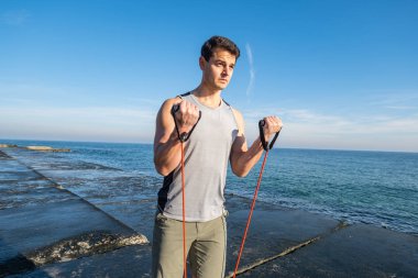 Young fit male training with  athletic rubber on the beach in summer day