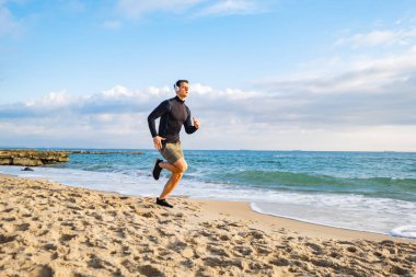 Fit male runner training on the summer beach and listen to music against beautidul sky and sea