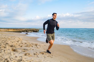 Fit male runner training on the summer beach and listen to music against beautidul sky and sea