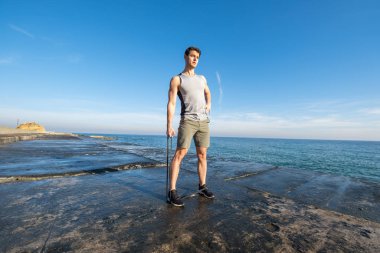 Young fit male training with  athletic rubber on the beach in summer day