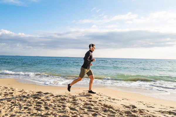 Fit Αρσενικό Δρομέας Κατάρτισης Στην Παραλία Του Καλοκαιριού Και Ακούσετε — Φωτογραφία Αρχείου