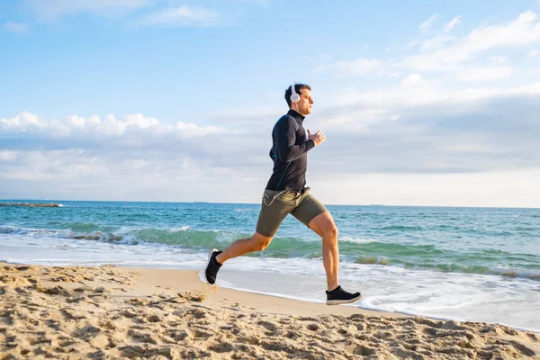 Fit male runner training on the summer beach and listen to music against beautidul sky and sea