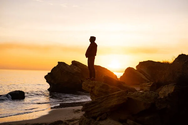 silhouette of male traveler stand near cliff and watch beautiful sunset in the sea