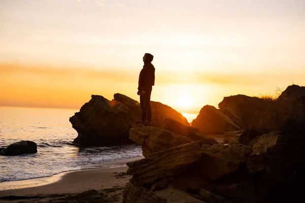 silhouette of male traveler stand near cliff and watch beautiful sunset in the sea