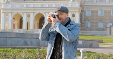 Elinde film kamerası olan genç ve yakışıklı bir gezgin sokak fotoğrafları çekiyor.