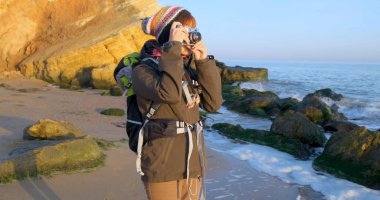 Sırt çantası ve retro film kamerasıyla genç bayan gezgin deniz kenarındaki sonbahar dağlarında seyahat ediyor.