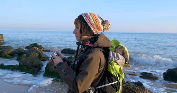 Sırt çantası ve retro film kamerasıyla genç bayan gezgin deniz kenarındaki sonbahar dağlarında seyahat ediyor.