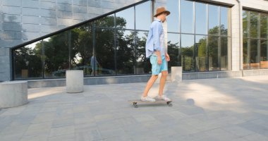 Şehirde kaykaylı yakışıklı bir erkek kulaklıkla müzik dinliyor.