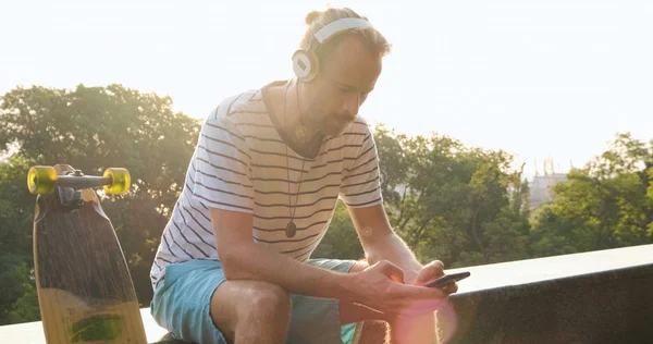 Şehirde Kaykaylı Yakışıklı Bir Erkek Kulaklıkla Müzik Dinliyor — Stok fotoğraf