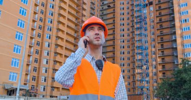 Turuncu miğfer ve güvenlik yeleği konusunda uzman birinin portresi büyük binaya karşı.