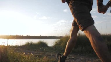 Young happy couple of lovers hiking near river in summer time against beautiful sunset