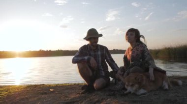 happy young couple play with corgi dog on the river beach against the sunset