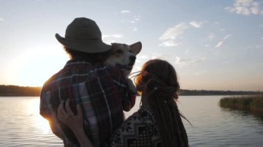 happy young couple play with corgi dog on the river beach against the sunset