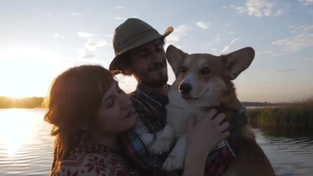 Щаслива Молода Пара Грає Коргі Собакою Березі Річки Проти Заходу — стокове відео