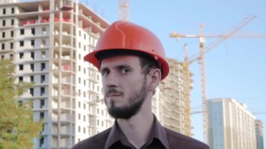 Turuncu miğfer ve güvenlik yeleği konusunda uzman birinin portresi büyük binaya karşı.