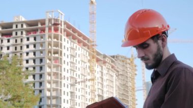 Turuncu miğfer ve güvenlik yeleği konusunda uzman birinin portresi büyük binaya karşı.