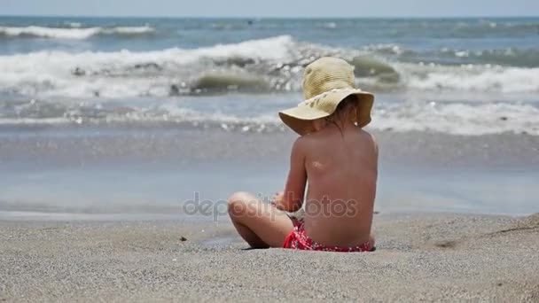Malá dívka sedící na pláži — Stock video