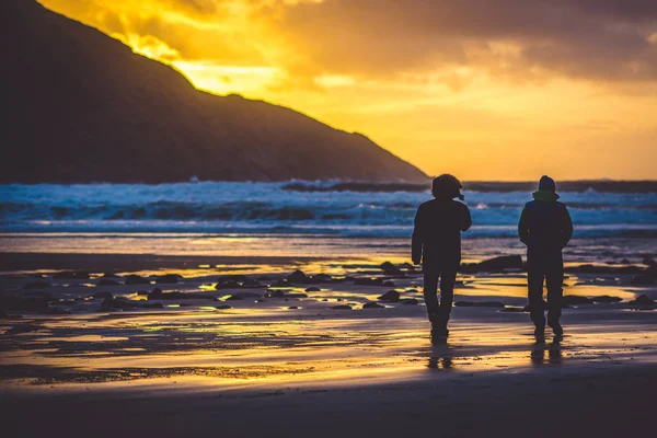 Back view to the people standing on coast near the sea on sunset