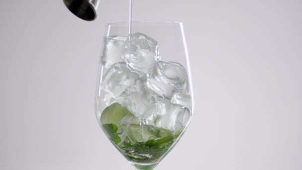 Il liquido viene versato in un bicchiere con cubetti di ghiaccio e foglie di lime e menta . — Video Stock