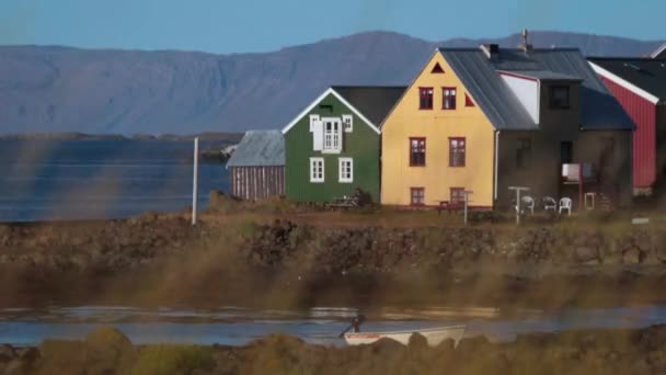 Человек сидит на скамейке рядом с красочными исландскими домами. Андреев . — стоковое видео