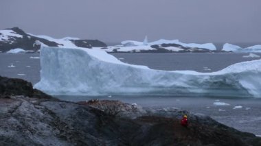 Kırmızı giysili bir adam bir taşa oturur ve buzullar görünüyor. Andreev.