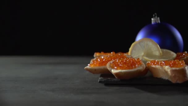 Sandwiches con caviar se encuentran en un stand decorado con un limón en rodajas contra un juguete árbol de Navidad azul . — Vídeo de stock