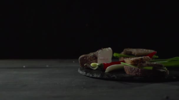 Zout en kruiden worden gegoten op brood met spek, paprika en uien. — Stockvideo