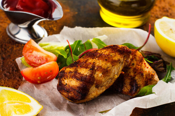 Grilled chicken breast with vegetables and salad over dark background. Selective focus