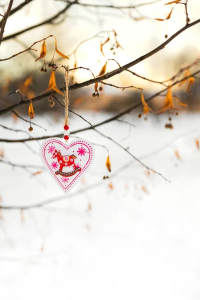 Valentín en forma de corazón o juguete de decoración de Navidad colgado en la rama del árbol con nieve en el fondo — Foto de Stock