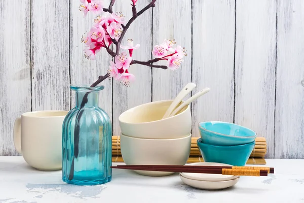 Japanse keukengerei, serviesgoed, stokjes en tak van bloeiende sakura op witte Aziatische achtergrond — Stockfoto
