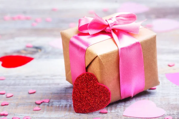 Подарочная коробка с розовой лентой и блестящими сердцами на деревенском фоне — стоковое фото