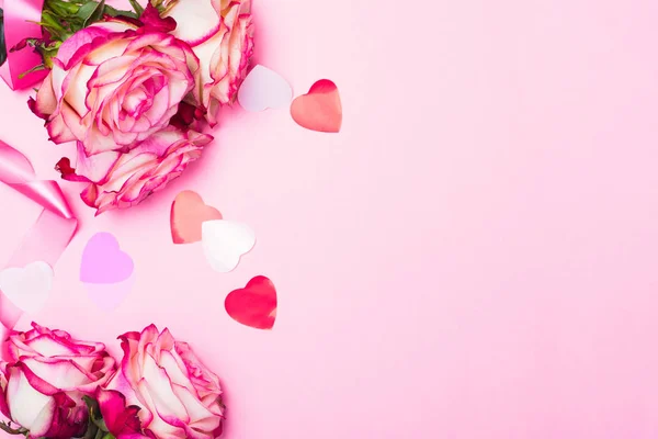 Krásné růžové růže, dekorativní konfety srdce a růžová stuha na růžovém pozadí Valentýn — Stock fotografie