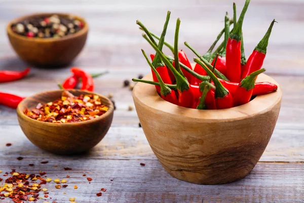 Gousses de piment rouge dans un mortier en bois, flocons de poivre et grains de poivre dans des bols en bois — Photo