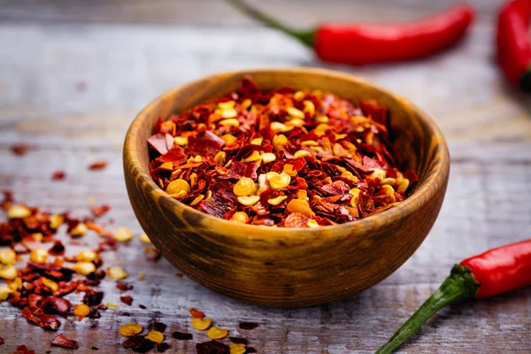 Flocons de piment rouge dans un mortier en bois et des gousses de poivre sur une table en bois — Photo