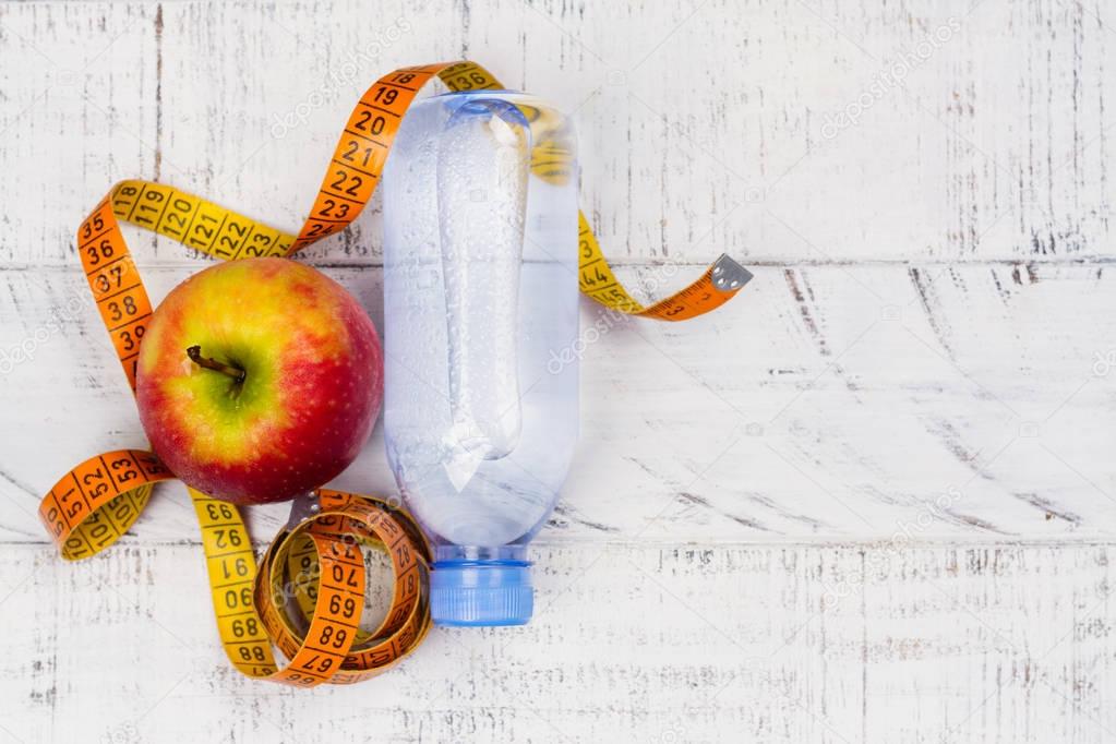 Apple, bottle of water and measuring tape on white background