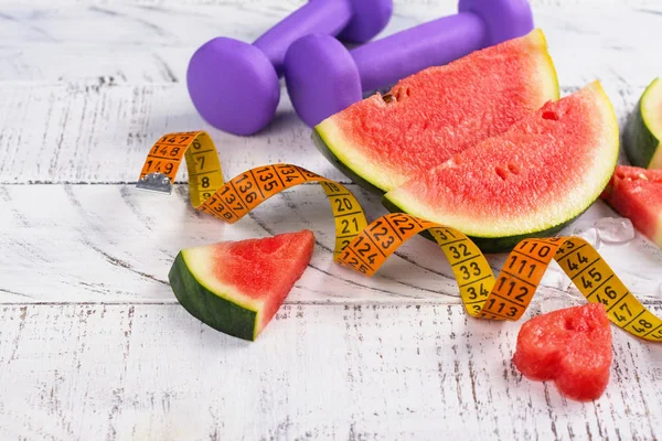 Frische reife Wassermelonenscheiben, Hanteln und Maßband auf Holzgrund — Stockfoto