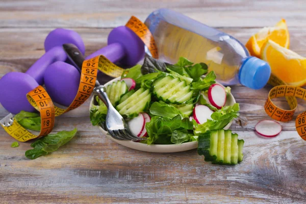 Ensalada vegetariana saludable, pesas y botella de agua en la mesa de madera —  Fotos de Stock