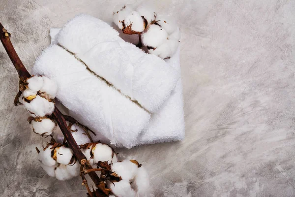 Pila de toallas de algodón, rama con flores de algodón, jabón y vela de té sobre fondo de piedra gris —  Fotos de Stock